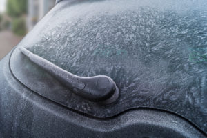 Close up view of a frozen car rear window. Ice covered windshield wipers and car windscreen.